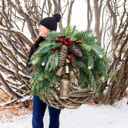 Frau trägt den Weihnachtskranz mit Glöckchen im verschneiten Garten