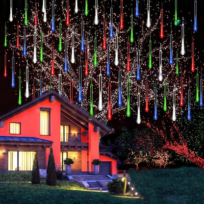 Mehrfarbige Meteorschauer-Lichterkette in einem Baum vor einem beleuchteten Haus