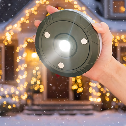 Hand hält die LED-Lampe vor einem Haus mit Weihnachtslichtern